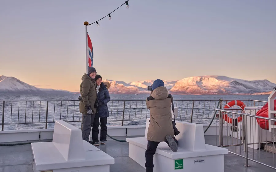 Passengers on the deck of a fjord cruise boat near Tromso at dusk